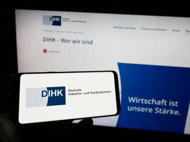 Stuttgart, Almanya - 03-24-2023: Web sayfası önünde üzerinde Deutsche Industrie- und Handelskammer (DIHK) logosu olan cep telefonu sahibi kişi. Telefon ekranına odaklan.