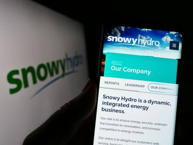 Stuttgart, Germany - 03-25-2023: Person holding cellphone with webpage of Australian energy company Snowy Hydro Limited on screen with logo. Focus on center of phone display. clipart