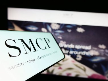 Stuttgart, Almanya - 03-25-2023: Fransız lüks moda şirketi SMCP SA 'nın logosuna sahip akıllı telefon iş dünyasının web sitesinin önünde ekranda. Telefon ekranının merkez soluna odaklan.