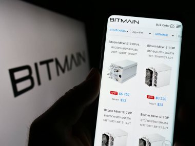 Stuttgart, Almanya - 03-25-2023: Çinli Bitmain Technologies Ltd. adlı şirketin internet sayfası ile logo önünde cep telefonu tutan kişi. Telefon ekranının merkezine odaklan.