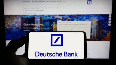 Stuttgart, Almanya - 03-25-2023: Alman finans şirketi Deutsche Bank AG 'nin logosuyla cep telefonu sahibi olan kişi iş sayfasının önünde ekranda görülüyor. Telefon ekranına odaklan.