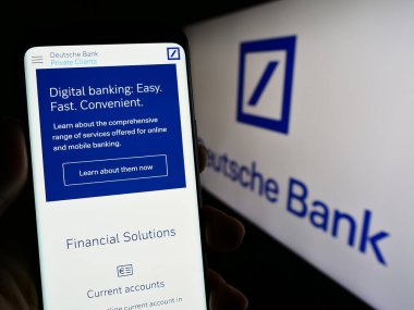Stuttgart, Almanya - 03-25-2023: Alman finans şirketi Deutsche Bank AG 'nin internet sayfası ile akıllı telefon sahibi kişi logonun önünde ekranda. Telefon ekranının merkezine odaklan.