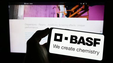 Stuttgart, Germany - 03-25-2023: Person holding smartphone with logo of German chemical company BASF SE on screen in front of website. Focus on phone display. clipart