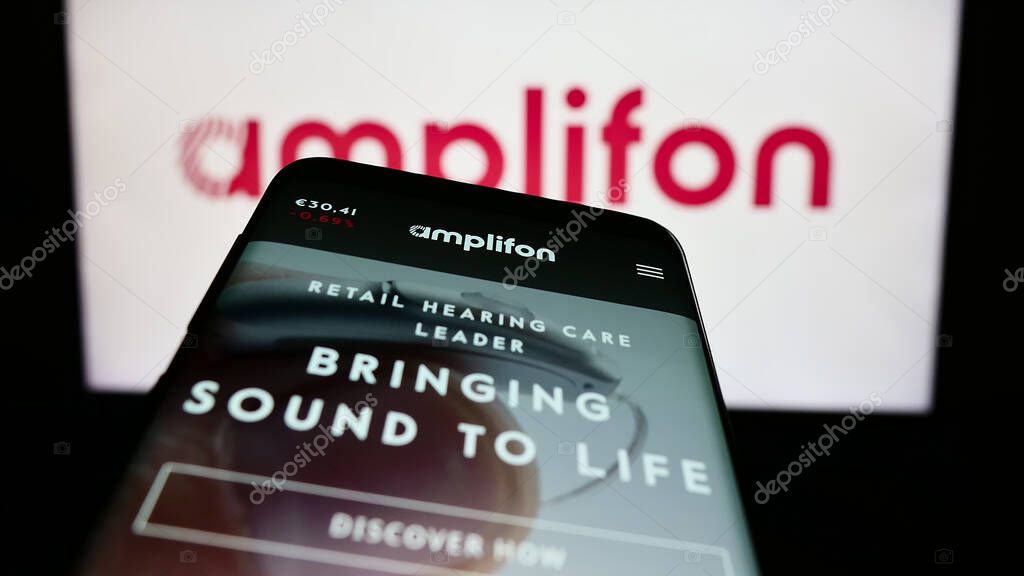 Stuttgart, Germany - 03-25-2023: Smartphone with website of Italian hearing aid company Amplifon S.p.A. on screen in front of business logo. Focus on top-left of phone display.