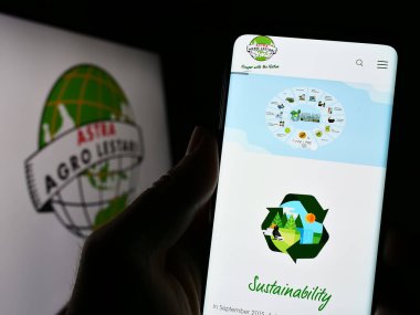 Stuttgart, Almanya - 03-25-2023: Endonezyalı PT Astra Agro Lestari Tbk 'in web sitesi ile cep telefonu tutan kişi logolu ekranda. Telefon ekranının merkezine odaklan.