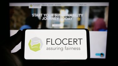 Stuttgart, Almanya - 03-25-2023: Ürün sertifika kurumu FLOCERT GmbH logosuna sahip akıllı telefonu web sitesi önünde ekranda tutan kişi. Telefon ekranına odaklan.