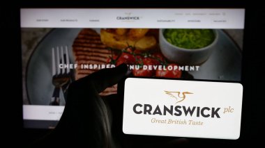 Stuttgart, Almanya - 01-17-2025: İngiliz gıda şirketi Cranswick 'in logosunun bulunduğu cep telefonu sahibi kişi iş sayfasının önünde ekranda. Telefon ekranına odaklan.