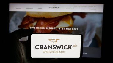 Stuttgart, Almanya - 01-17-2025: İngiliz gıda şirketi Cranswick plc 'in logosuyla cep telefonu sahibi kişi iş sayfasının önünde ekranda. Telefon ekranına odaklan.