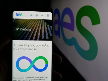 Stuttgart, Germany - 01-17-2025: Person holding smartphone with logo of US utility company AES Corporation on screen in front of website. Focus on phone display. clipart