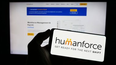 Stuttgart, Germany - 03-25-2023: Person holding mobile phone with logo of Australian software company Humanforce on screen in front of business web page. Focus on phone display. clipart