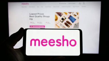 Stuttgart, Almanya - 03-26-2023: Hint e-ticaret şirketi Meesho 'nun logosunu elinde tutan kişi web sitesinin önünde ekranda. Telefon ekranına odaklan.