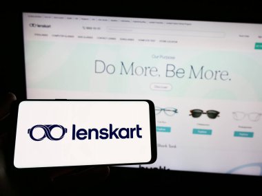 Stuttgart, Germany - 03-26-2023: Person holding smartphone with logo of Indian eyewear company Lenskart on screen in front of website. Focus on phone display. clipart