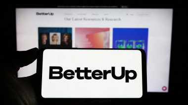 Stuttgart, Almanya - 03-26-2023: Amerikan koçluk şirketi BetterUp 'ın logosunu taşıyan cep telefonu sahibi kişi iş sayfasının önünde ekranda. Telefon ekranına odaklan.