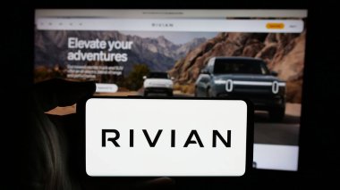 Stuttgart, Almanya - 01-20-2025: İnternet sayfasının önünde üzerinde elektrikli araç şirketi Rivian Automotive Inc. 'in logosu olan cep telefonu bulunduran kişi. Telefon ekranına odaklan.