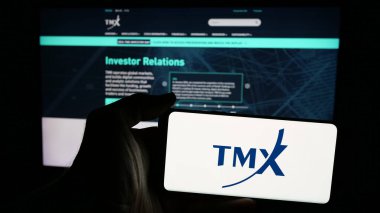 Stuttgart, Germany - 01-20-2025: Person holding mobile phone with logo of Canadian stock exchange company TMX Group Limited on screen in front of web page. Focus on phone display. clipart