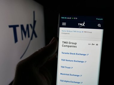 Stuttgart, Germany - 01-20-2025: Person holding cellphone with webpage of Canadian stock exchange company TMX Group Limited on screen with logo. Focus on center of phone display. clipart