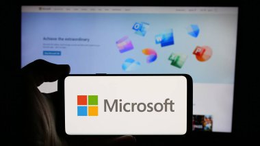 Stuttgart, Almanya - 01-20-2025: ABD 'li teknoloji şirketi Microsoft Corporation' ın logosuyla cep telefonu sahibi kişi iş sayfasının önünde ekranda. Telefon ekranına odaklan.