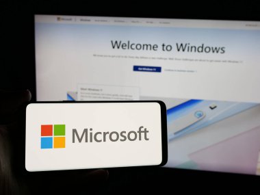 Stuttgart, Almanya - 01-20-2025: ABD 'li teknoloji şirketi Microsoft Corporation' ın logosunu elinde tutan kişi web sitesinin önünde ekranda. Telefon ekranına odaklan.