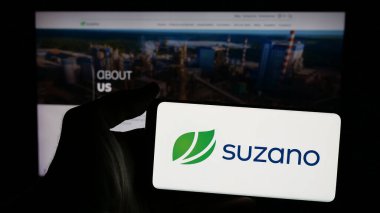 Stuttgart, Almanya - 01-20-2025: Brezilya hamuru ve kağıt şirketi Suzano SA 'nın logosu olan cep telefonu sahibi kişi iş sayfasının önünde ekranda. Telefon ekranına odaklan.