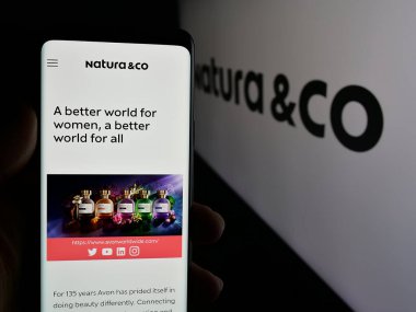 Stuttgart, Almanya - 01-23-2025: Brezilyalı kozmetik şirketi Natura Co Holding S.A. 'nın web sayfası ile cep telefonu tutan kişi logo ile ekranda. Telefon ekranının merkezine odaklan.