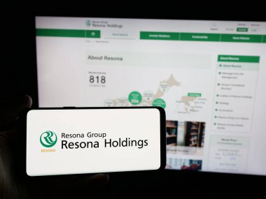 Stuttgart, Almanya - 01-23-2025: Japon bankacılık şirketi Resona Holding Inc. 'nin logosunu elinde tutan kişi web sitesinin önünde ekranda. Telefon ekranına odaklan.