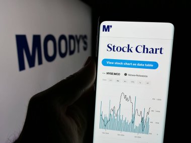 Stuttgart, Almanya - 01-23-2025: ABD 'li finans şirketi Moody' s Corporation 'ın web sayfası ile logo önünde cep telefonu tutan kişi. Telefon ekranının merkezine odaklan.