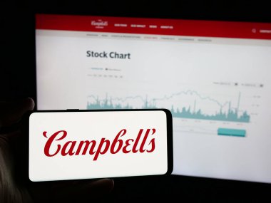 Stuttgart, Almanya - 01-23-2025: ABD gıda işleme şirketinin logosuna sahip akıllı telefonu olan kişi The Campbell 's Company web sitesinin önünde ekranda. Telefon ekranına odaklan.