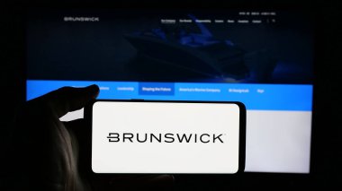 Stuttgart, Almanya - 01-23-2025: ABD 'li deniz şirketi Brunswick Corporation' ın logosuyla cep telefonu sahibi kişi iş sayfasının önünde ekranda. Telefon ekranına odaklan.