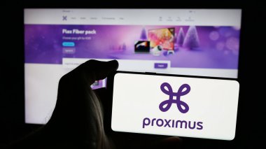 Stuttgart, Germany - 01-28-2025: Person holding mobile phone with logo of Belgian telecommunications company Proximus Group on screen in front of web page. Focus on phone display. clipart