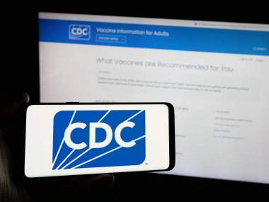 Stuttgart, Almanya - 01-28-2025: İnternet sitesi önünde üzerinde Hastalık Kontrol ve Önleme Merkezleri (CDC) logosu bulunan kişi. Telefon ekranına odaklan.