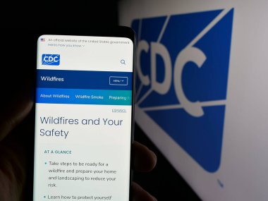 Stuttgart, Germany - 01-28-2025: Person holding cellphone with webpage of Centers for Disease Control and Prevention (CDC) on screen with logo. Focus on center of phone display. clipart