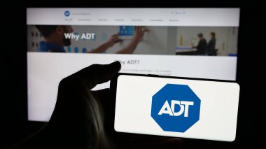 Stuttgart, Almanya - 01-28-2025: Amerikan güvenlik şirketi ADT Inc. 'nin logosunun bulunduğu cep telefonu sahibi kişi iş sayfasının önünde ekranda. Telefon ekranına odaklan.