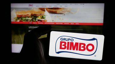 Stuttgart, Almanya - 01-28-2025: Meksikalı gıda şirketi Grupo Bimbo S.A.B. 'nin logosuyla cep telefonu tutan kişi de C.V. web sayfasının önünde ekranda. Telefon ekranına odaklan.