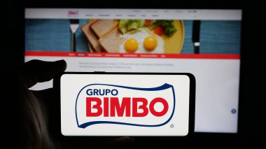 Stuttgart, Almanya - 01-28-2025: Meksikalı gıda şirketi Grupo Bimbo SAB de CV 'nin logosuyla cep telefonu sahibi kişi iş sayfasının önünde ekranda. Telefon ekranına odaklan.