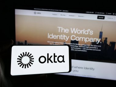 Stuttgart, Almanya - 01-29-2025: Web sitesinin önünde ekranda ABD 'li kimlik yönetim şirketi Okta Inc.' nin logosuna sahip akıllı telefonu tutan kişi. Telefon ekranına odaklan.