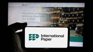 Stuttgart, Almanya - 01-29-2025: ABD 'li Uluslararası Kağıt Şirketi' nin logosuyla cep telefonu sahibi kişi iş sayfasının önünde ekranda. Telefon ekranına odaklan.