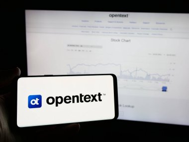 Stuttgart, Germany - 01-30-2025: Person holding smartphone with logo of Canadian software company OpenText Corporation on screen in front of website. Focus on phone display. clipart