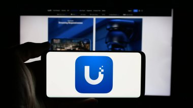 Stuttgart, Almanya - 01-30-2025: ABD 'li teknoloji şirketi Ubiquiti Inc.' in logosuyla cep telefonu sahibi kişi iş sayfasının önünde ekranda. Telefon ekranına odaklan.