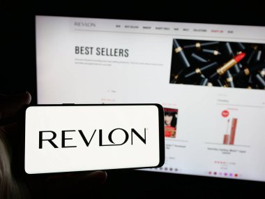 Stuttgart, Almanya - 01-30-2025: ABD 'li kozmetik şirketi Revlon Inc.' in logosunu elinde tutan kişi web sitesinin önünde ekranda. Telefon ekranına odaklan.