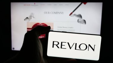 Stuttgart, Almanya - 01-30-2025: Amerikan kozmetik şirketi Revlon Inc. 'in logosu olan cep telefonu sahibi kişi iş sayfasının önünde ekranda. Telefon ekranına odaklan.