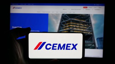 Stuttgart, Germany - 01-30-2025: Person holding cellphone with logo of Mexican materials company CEMEX SAB de CV on screen in front of business webpage. Focus on phone display. clipart