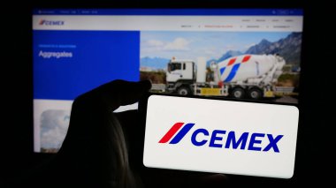 Stuttgart, Almanya - 01-30-2025: Üzerinde Meksikalı malzeme şirketi CEMEX S.A.B. logosu olan cep telefonu tutan kişi de C.V. web sayfasının önünde ekranda. Telefon ekranına odaklan.