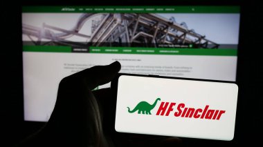 Stuttgart, Germany - 01-30-2025: Person holding mobile phone with logo of American energy company HF Sinclair Corporation on screen in front of web page. Focus on phone display. clipart