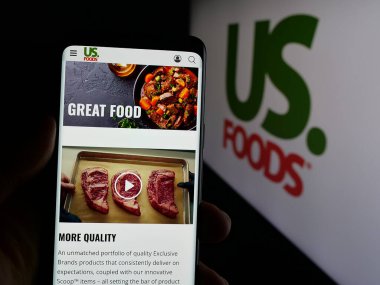 Stuttgart, Almanya - 01-31-2025: İnternet sitesinin önünde ekranda US Foods Holding Corp. 'un logosunun bulunduğu akıllı telefonu tutan kişi. Telefon ekranına odaklan.