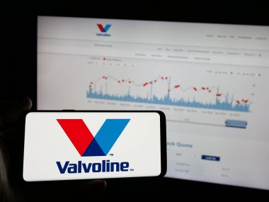 Stuttgart, Germany - 01-31-2025: Person holding smartphone with logo of US automotive services company Valvoline Inc. on screen in front of website. Focus on phone display. clipart