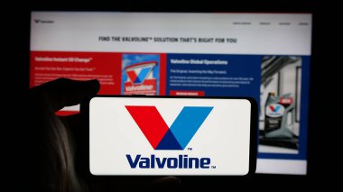 Stuttgart, Germany - 01-31-2025: Person holding cellphone with logo of American automotive services company Valvoline Inc. on screen in front of webpage. Focus on phone display. clipart