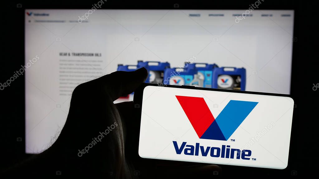 Stuttgart, Germany - 01-31-2025: Person holding mobile phone with logo of US automotive services company Valvoline Inc. on screen in front of web page. Focus on phone display.