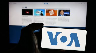 Stuttgart, Almanya - 01-31-2025: İnternet sayfası önünde ABD yayın ağı Voice of America 'nın (VOA) logosuna sahip cep telefonu sahibi kişi. Telefon ekranına odaklan.