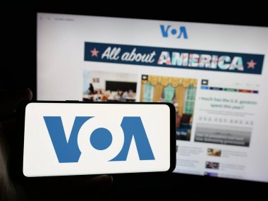 Stuttgart, Almanya - 01-31-2025: İnternet sitesi önünde ekranda ABD yayın ağı Voice of America 'nın (VOA) logosunu taşıyan kişi. Telefon ekranına odaklan.