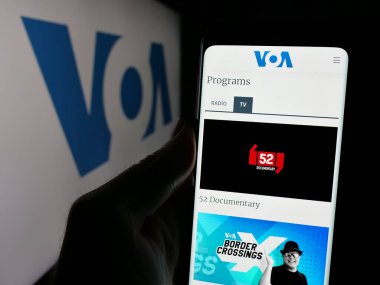 Stuttgart, Almanya - 01-31-2025: ABD yayın ağı Voice of America 'nın (VOA) web sayfası bulunan cep telefonu logolu kişi. Telefon ekranının merkezine odaklan.